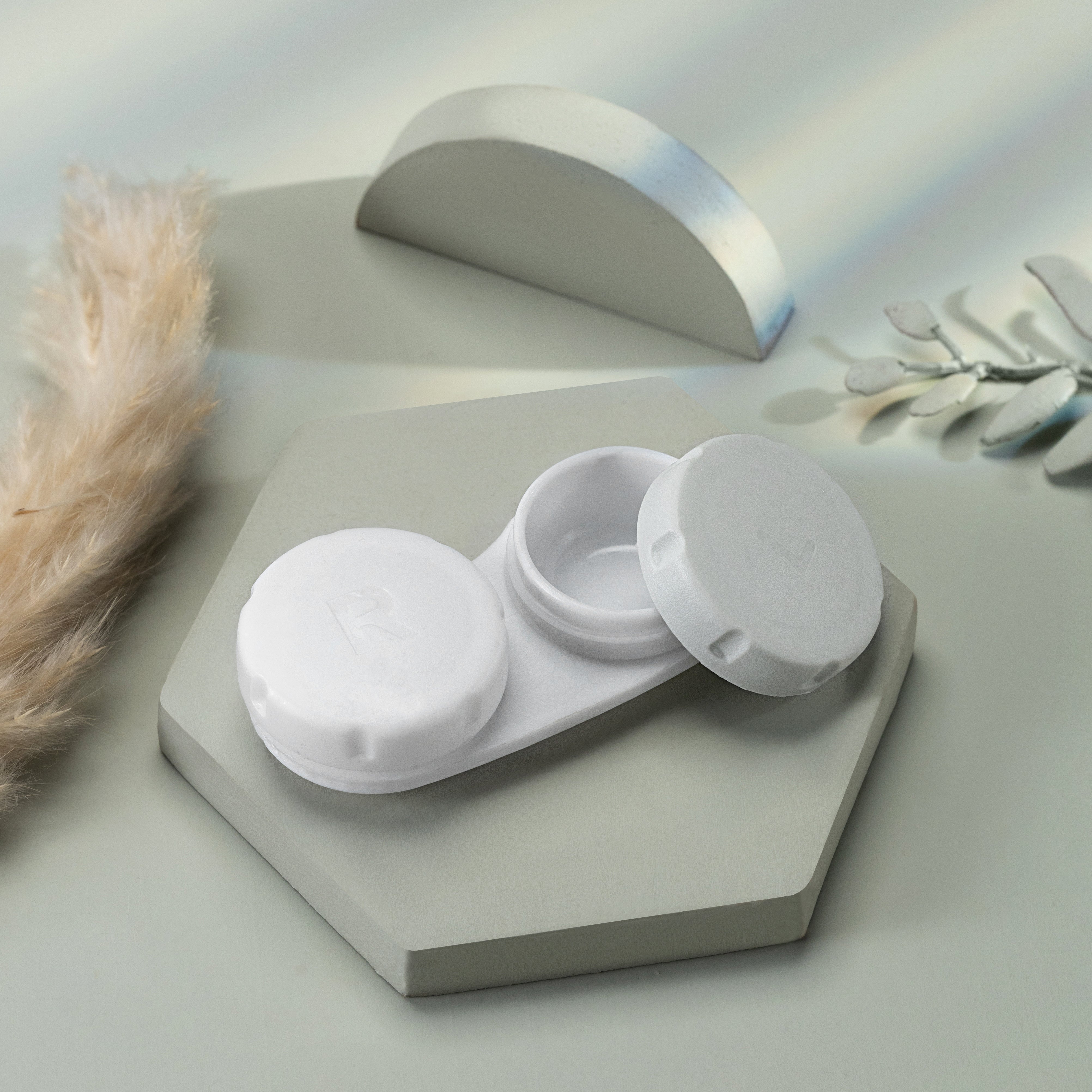 White contact lens case on a light gray surface with decorative elements.